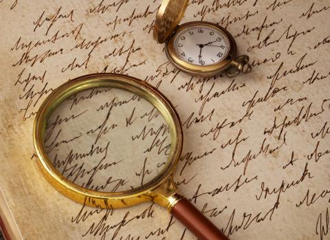 Magnifying glass and pocket watch atop parchment with script