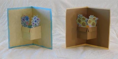 Two cards standing up side-by-side made with recycled paper, a pop-out element at the crux of the card's central fold creating the semblance of a flower pot out of which emerge colorful illustrated two-dimensional flowers