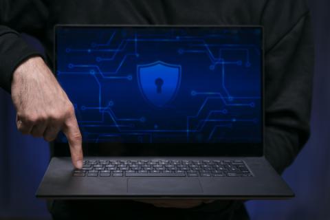 Laptop in a dark room pointed towards the screen which showcases a lock symbol, a hand poised over the keyboard