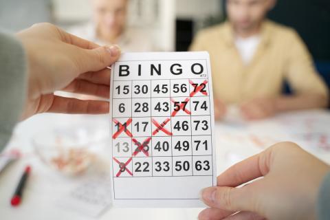 Close-up of hand holding a Bingo card with items diagonally crossed out in red