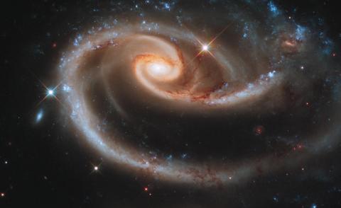 NASA Hubble Space Telescope image of a pair of interacting galaxies called "Arp 273," made up of "UGC 1810" caught in the pull of companion galaxy "UGC 1813" forming a rose-like spiral of gold within the dark space backdrop.