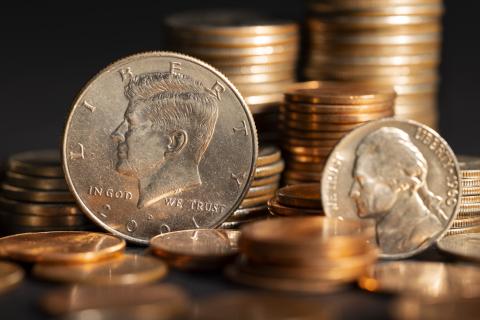 Stacks of American coinage laid out upon a table with two coins propped up in the foreground - one featuring John F. Kennedy, one featuring Thomas Jefferson