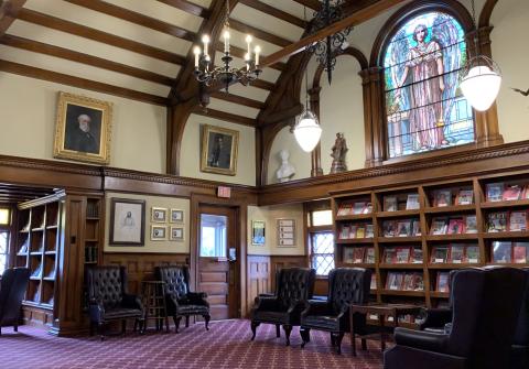 Emma S. Clark Library historic interior architecture - featuring magazine shelving, rich wood detailing, stained glass window, and maroon patterned carpet