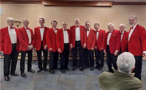 Long line of singers from "The Harbormen Chorus" in red jackets standing in the Emma Clark Library's Community Room