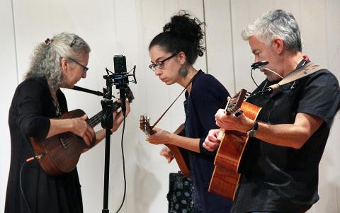 Trio of string music players from the "Homegrown String Band" standing around a microphone