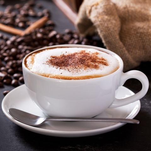 Photograph of a mug of espresso with thick foam and cinnamon on top, an overfull bag of coffee beans spilling out atop the table in the backdrop.