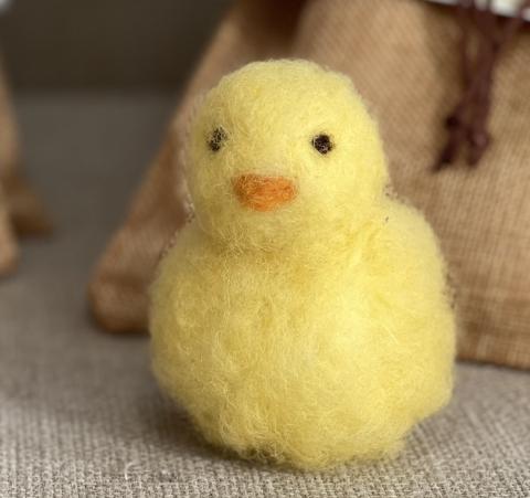 Needle-felted stylized chick, comprised of two yellow fluffy orbs one atop the other, a little orange beak, and two tiny black eyes.