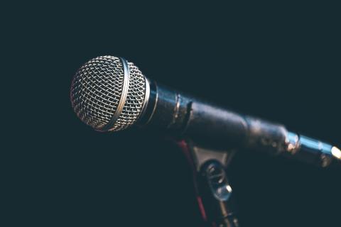 Close-up photograph of a standard microphone on a mic stand in front of a lack backdrop