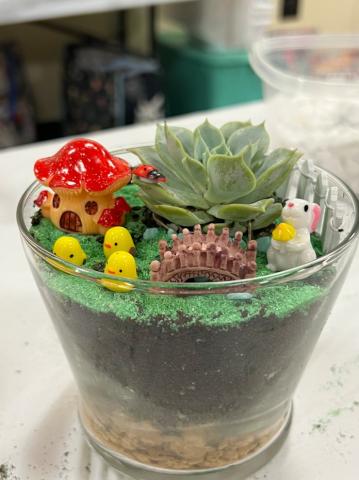 Glass container housing a small succulent surrounded by little accessories, including a miniature mushroom house, a rabbit, and three little chicks.