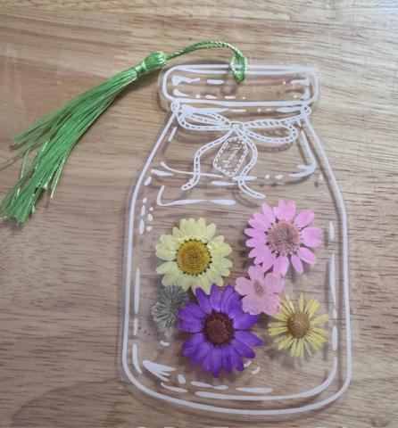 Craft bookmark of pressed flowers in a clear laminate shaped to look like a lass mason jar, with a green tassel looped at the top