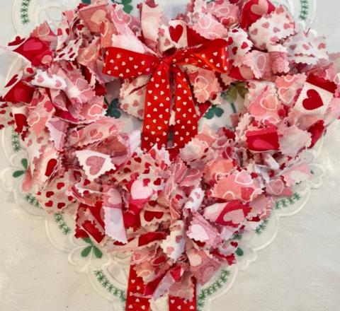 Heart-shaped wreath, made up of a series of ribbons in pink, white, and red with heart-shaped designs.