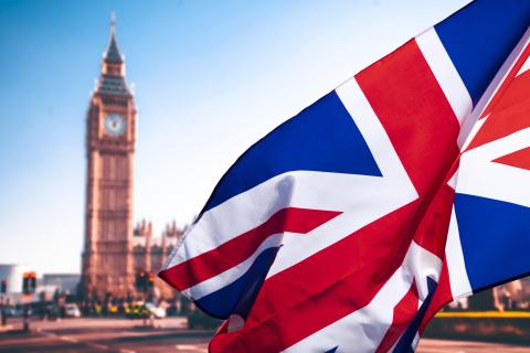 Photograph of London's "Big Ben" clock tower viewed blurred at a distance, while in the foreground the English Union Jack flag waves dramatically.