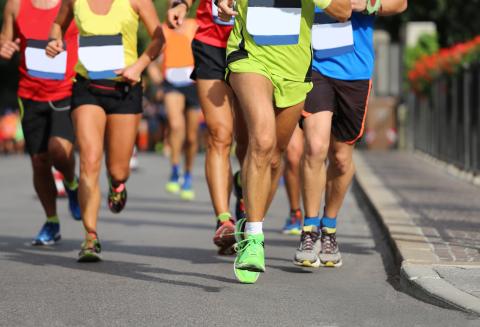 Photograph of a group of athletes in vibrant tracksuits as viewed from the waist down running along a paved street