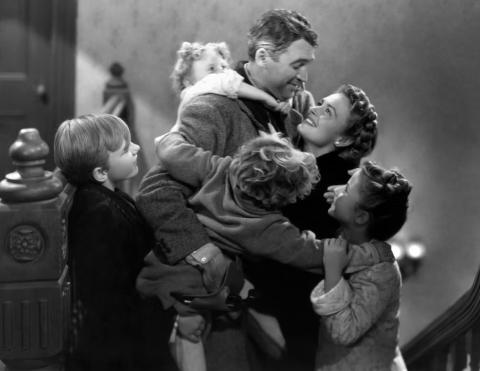 Screenshot from Frank Capra’s classic holiday film "It’s a Wonderful Life," depicting the leading man as portrayed by Jimmy Stewart embracing his family, as seen at the triumphant end of the film