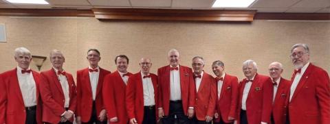 Photograph of the full Harbormen Chorus, made up of eleven elderly white men in matching red suits with white shirts and red bowties