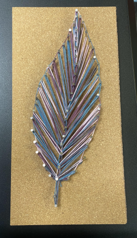 Photograph of a depiction of a feather created with pins and string in colors of blue and purple on a corkboard