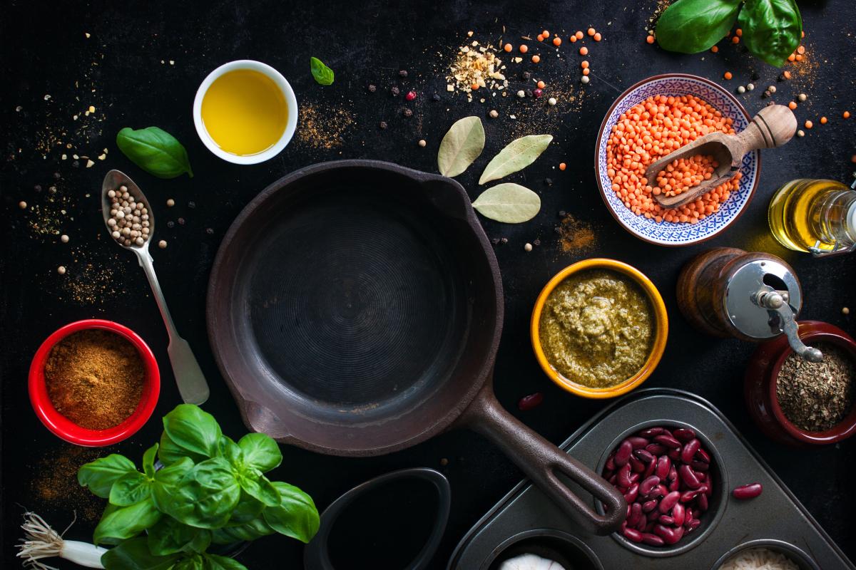 Frying pan and dishes of assorted vibrant spices laying atop a black marble countertop