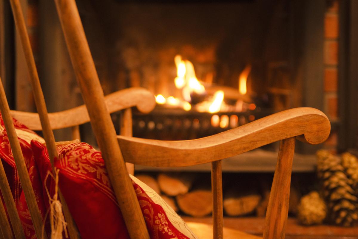 Close-up photo of a fireplace as viewed through the rungs of a rocking chair with red cushion in the foreground