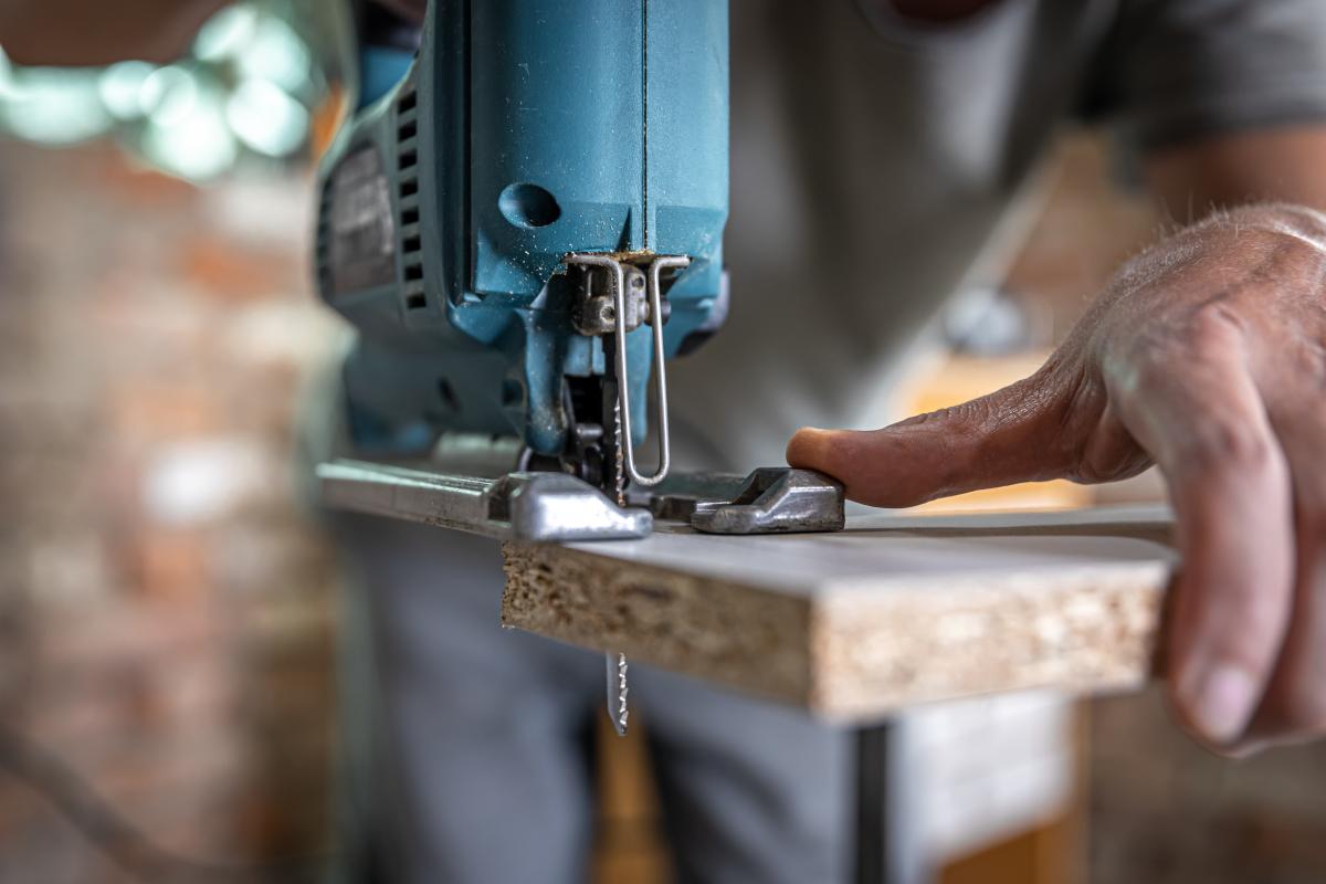 Close-up photograph of hands manipulating a handsaw on a plank of wood.